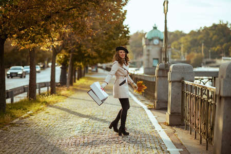 Hello october. Portrait of smiling stylish female in beige trench coat outside on the city street in autumn.の写真素材