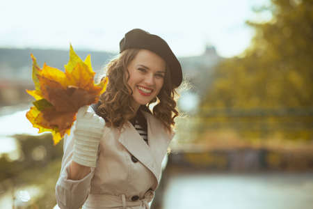 Hello october. Portrait of smiling stylish female in beige trench coat outside on the city street in autumn.の写真素材