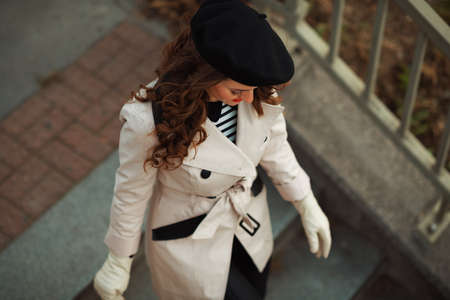 Hello october. Portrait of smiling stylish female in beige trench coat outside on the city street in autumn.の写真素材