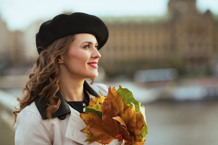 Hello october. Portrait of smiling stylish female in beige trench coat outside on the city street in...