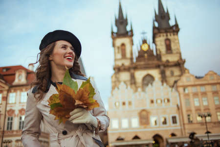 Hello october. Portrait of smiling stylish female in beige trench coat outside on the city street in autumn.の写真素材