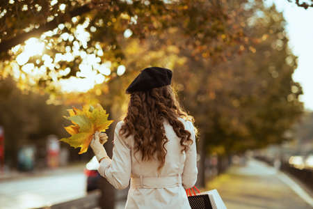 Hello september. smiling young woman in beige trench coat and black beret with autumn yellow leaves outside on the city street in autumn.の写真素材