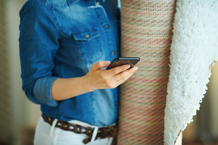 happy modern 40 years old woman in jeans shirt and white pants with pile of carpets searching for...