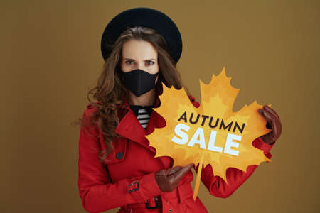 Life during coronavirus pandemic. stylish housewife in red coat with black mask, mug and paper shopping bags against bronze background.の写真素材