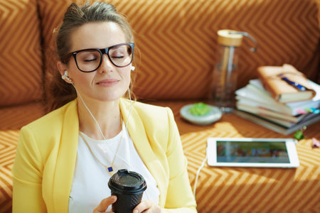 happy elegant female in yellow jacket with laptop and smartphone study online in the modern house in...