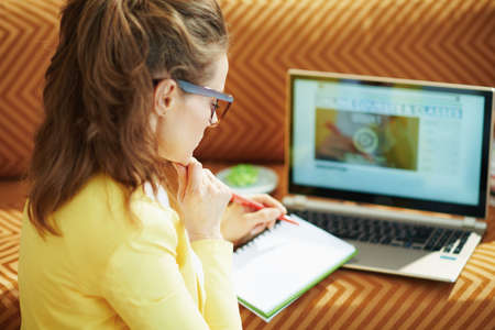 happy elegant female in yellow jacket with laptop and smartphone study online in the modern house in sunny day.の写真素材
