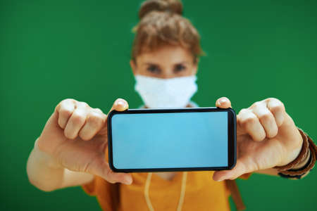 Life during coronavirus pandemic. Closeup on student woman with backpack putting additional medical mask in backpack isolated on green background.の写真素材