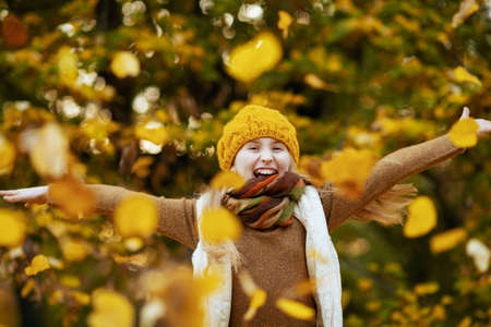 girl in brown sweater and orange hat rejoicing outdoors in the city park in autumn.の写真素材