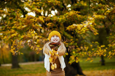 girl in brown sweater and orange hat rejoicing outdoors in the city park in autumn.の写真素材
