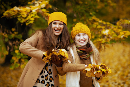 Hello autumn. Seen from behind modern mother and child in yellow hats with autumn yellow leaves...