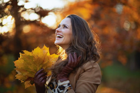 Hello autumn. Closeup on woman standing in boots on the green grass with autumn leaves outdoors in...