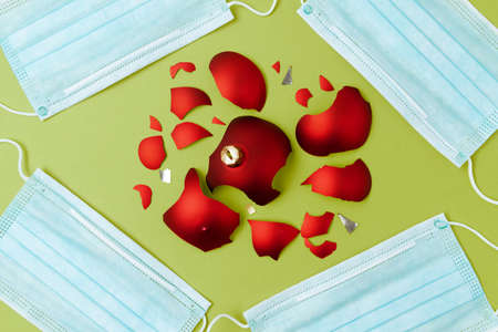 flat lay with medical mask and broken christmas ball on green background.の写真素材