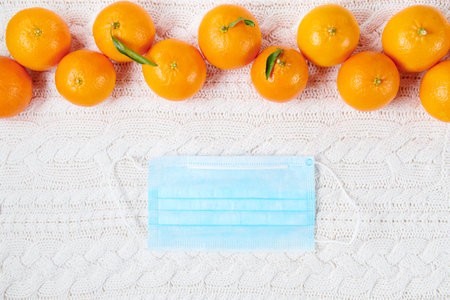 winter flat lay with medical mask and mandarins on white knitted background.の写真素材