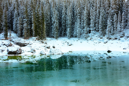 landscape with mountains, carezza lake, fir trees and clouds in Dolomites, Italy in winter.
