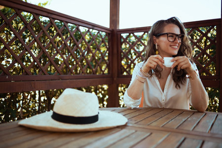 Portrait of happy modern female in white shirt with hat outdoors near green wall.の写真素材