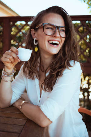 Portrait of happy modern female in white shirt with hat outdoors near green wall.の写真素材