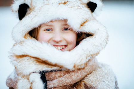 smiling stylish girl with mittens in a knitted hat and sheepskin coat playing outside in the city...