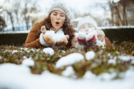 happy stylish mother and daughter in a knitted hats and sheepskin coats with medical mask in a knitted hat and sheepskin coat outside in the city park in winter.の写真素材