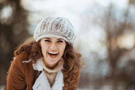 smiling elegant 40 years old woman with mittens and cup of tea in a knitted hat and sheepskin coat outside in the city park in winter.の写真素材