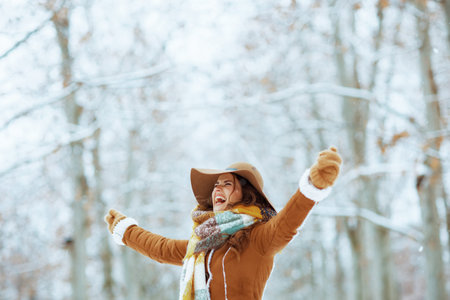 smiling elegant woman in brown hat and scarf outdoors in the city park in winter in sheepskin coat.
