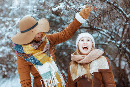 smiling elegant mother and child in hats and sheepskin coats with mittens playing outside in the city park in winter.の写真素材