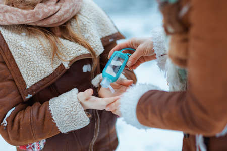 smiling elegant mother and child in hats and sheepskin coats with mittens playing outside in the city park in winter.の写真素材