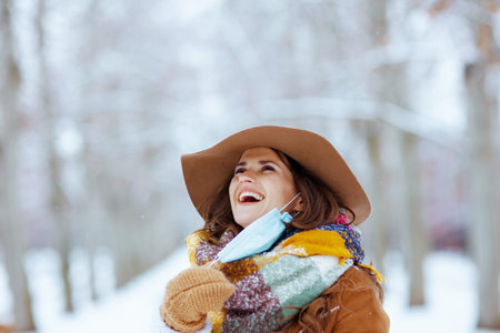 smiling stylish mother and child in hats and sheepskin coats disinfecting hands with sanitiser...