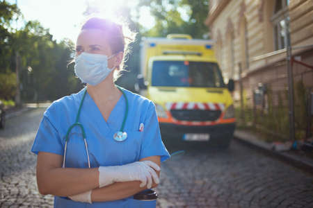 pandemic. modern medical doctor woman in scrubs with stethoscope and medical mask outdoors near ambulance.の写真素材