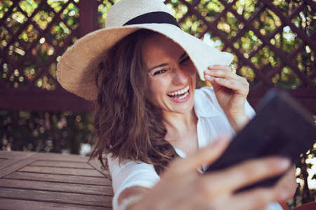 happy 40 years old woman in white shirt with hat using video chat on a smartphone in the terrace.の写真素材