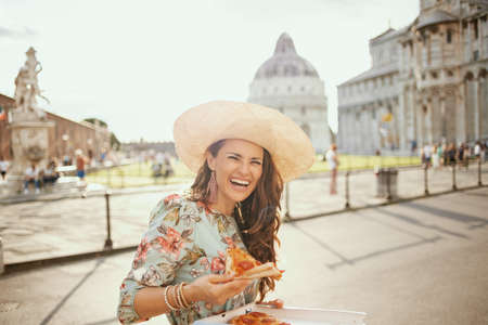 happy stylish solo tourist woman in floral dress with vintage camera and hat near Leaning Tower in Pisa, Italy.の写真素材