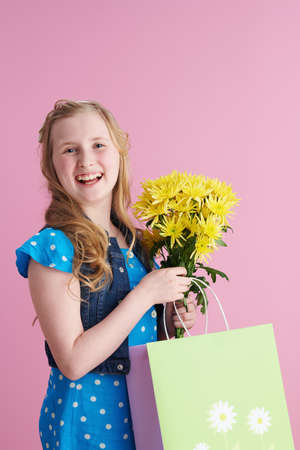happy stylish child with long wavy blond hair with yellow chrysanthemums flowers isolated on pink.の写真素材