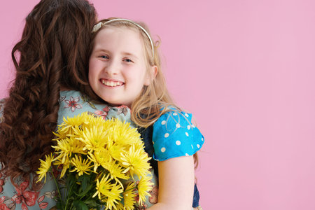 happy stylish mother and daughter with long wavy hair with yellow chrysanthemums flowers embracing...