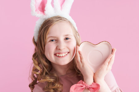 smiling stylish girl in pink dress with bunny ears showing thumbs up isolated on pink background.