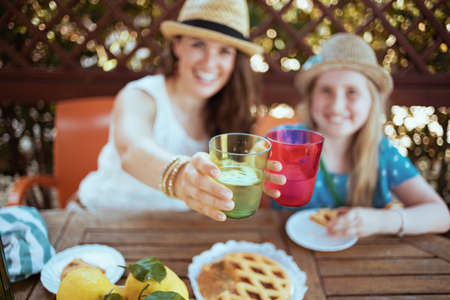 smiling modern mother and daughter with crostata, green bottle of water and plate of local farm lemons sitting at the table having lunch in the patio.の写真素材