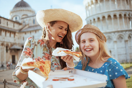 smiling stylish mother and daughter with pizza near Leaning Tower in Pisa, Italy.の写真素材