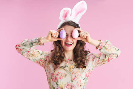 Closeup on woman with long wavy brunette hair with basket of easter eggs isolated on pink.の写真素材
