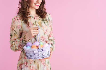 Closeup on woman with long wavy brunette hair with basket of easter eggs isolated on pink.の写真素材