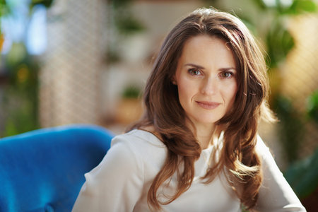 Green Home. stylish 40 years old woman with long wavy hair in the modern house in sunny day using video chat.の写真素材