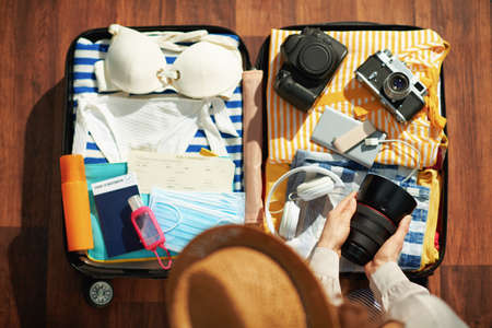 Upper view of 40 years old woman with antiseptic, wheel bag, air tickets, medical mask, spf, bikini and passport packing trolley bag in the modern living room in sunny day.の写真素材