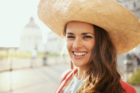 smiling young solo tourist woman in floral dress with vintage camera and hat near Cattedrale di Pisa.の写真素材