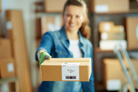 Delivery business. happy young female in jeans with parcels and packing tape dispenser in the warehouse.の写真素材