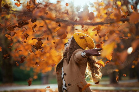 Hello september. smiling stylish woman in beige coat and orange hat with autumn yellow leaves outside in the city park in autumn.の写真素材