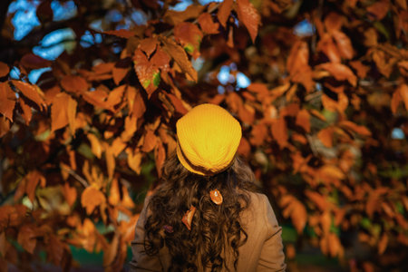 Hello september. smiling stylish woman in beige coat and orange hat with autumn yellow leaves outside in the city park in autumn.の写真素材