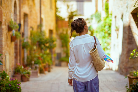 Travel in Italy. Seen from behind elegant tourist woman with straw bag having excursion in Pienza in Tuscany, Italy.の写真素材