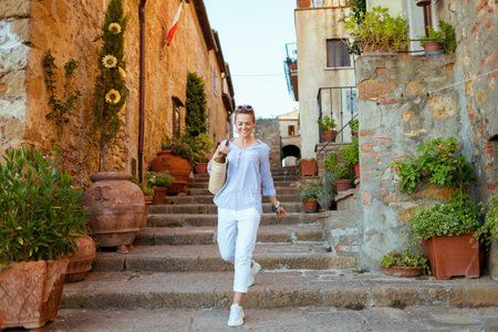 Travel in Italy. Seen from behind elegant tourist woman with straw bag having excursion in Pienza in...