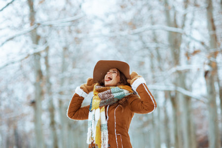 Closeup on woman in brown hat and scarf with mittens in sheepskin coat using hand cream outdoors in...