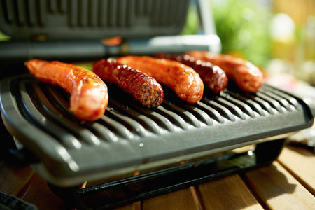 Summer backyard picnic. desk with electric grill and grilled sausages.