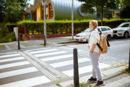 smiling trendy girl in white sweatshirt with workbook and backpack against wall outdoors in the city.の写真素材