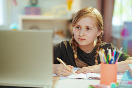 happy modern pupil in grey shirt with laptop and workbook having distance education and eating...