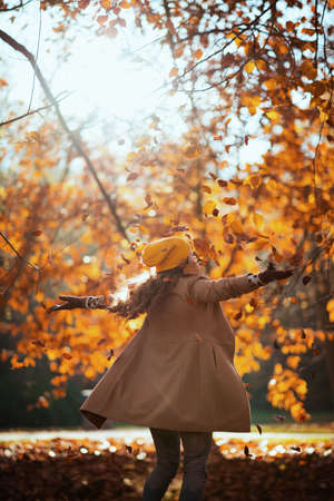 Hello september. happy trendy woman in brown coat and yellow hat having fun time outdoors in the city park in autumn.の写真素材
